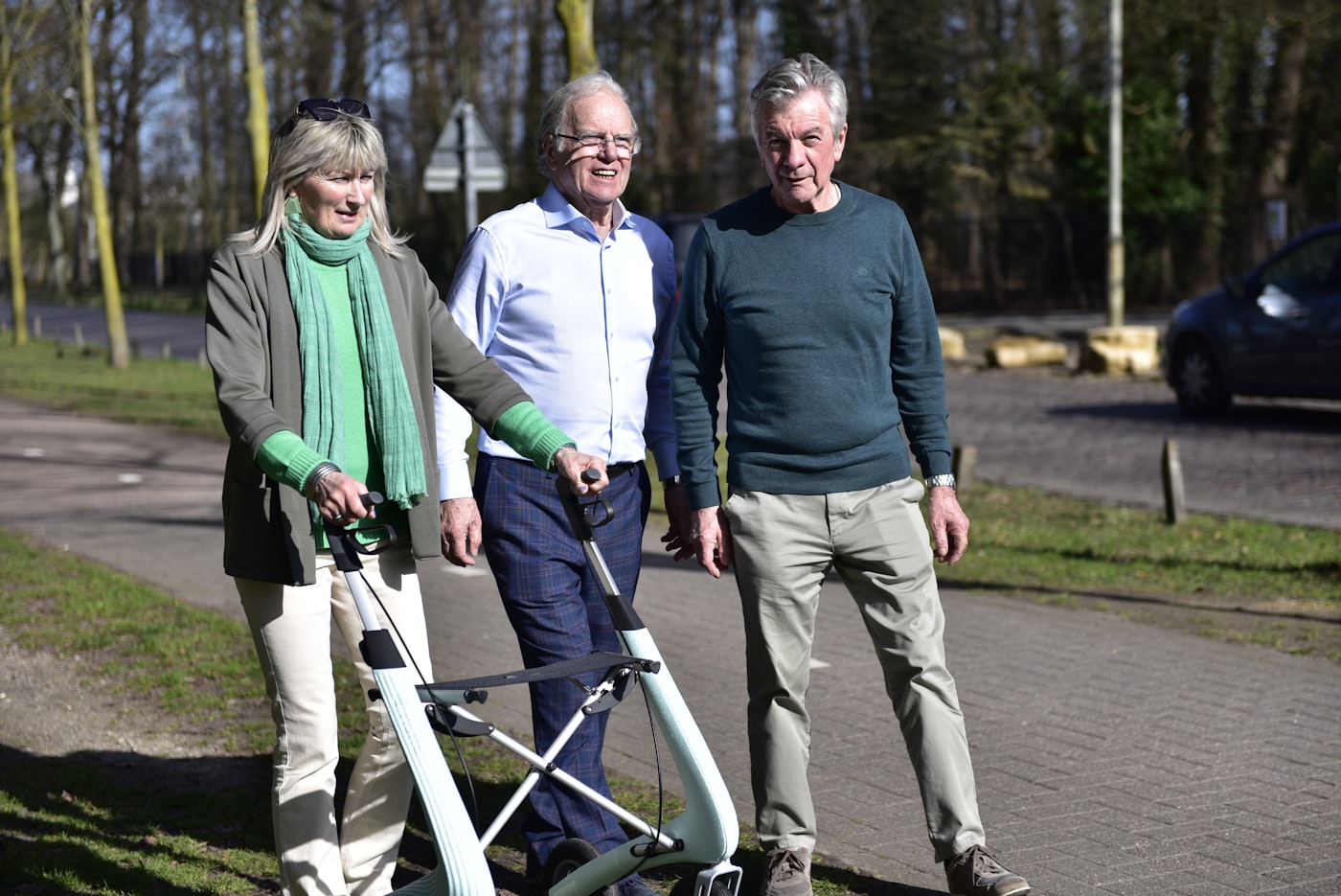 Three people walking outdoors with mobility walking frames